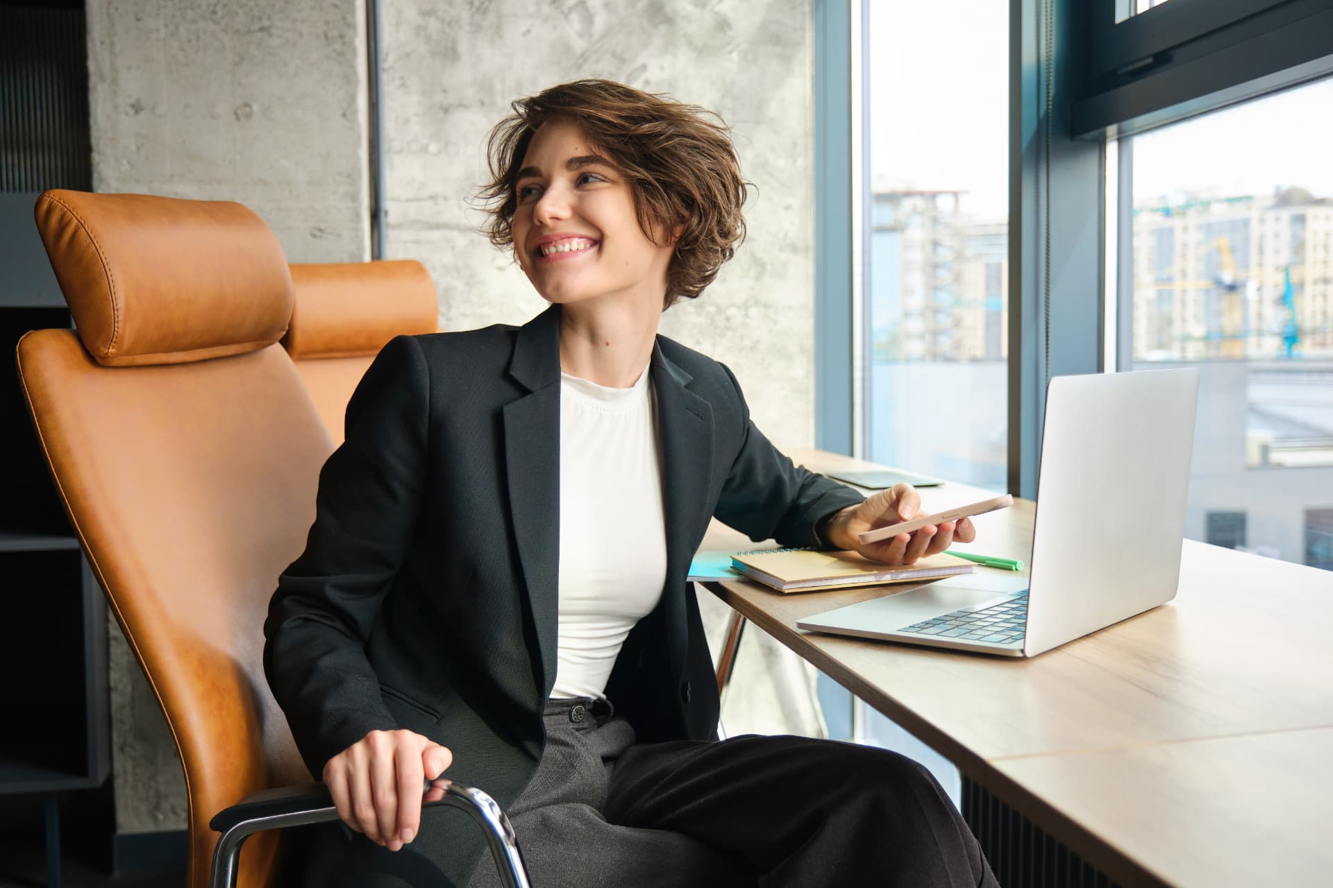 Corretora sorrindo no escritório com notebook e celular